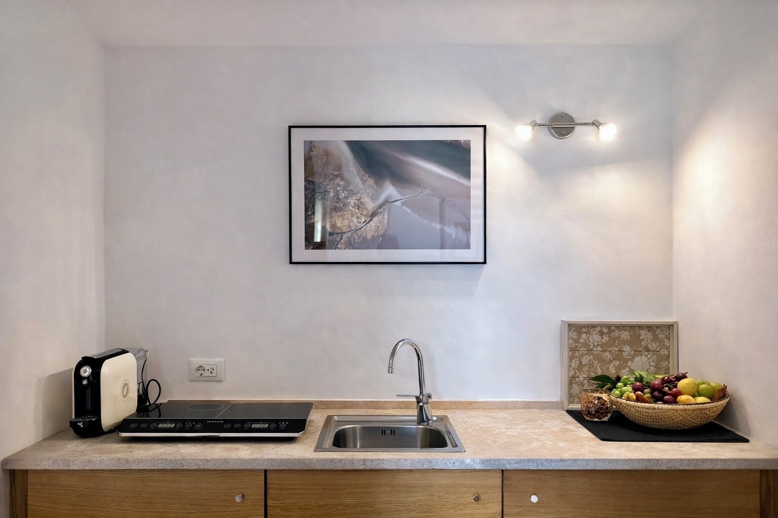 Une cuisine équipée d’une plaque de cuisson à induction intégrée, d’un évier en acier inoxydable et d’un panier à fruits posé sur le plan de travail.