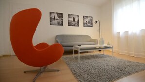 A modern living room with a red chair, grey sofa, and a white coffee table. There are three black-and-white photographs on the wall. - WeinheimResidence (2) (Weinheim)