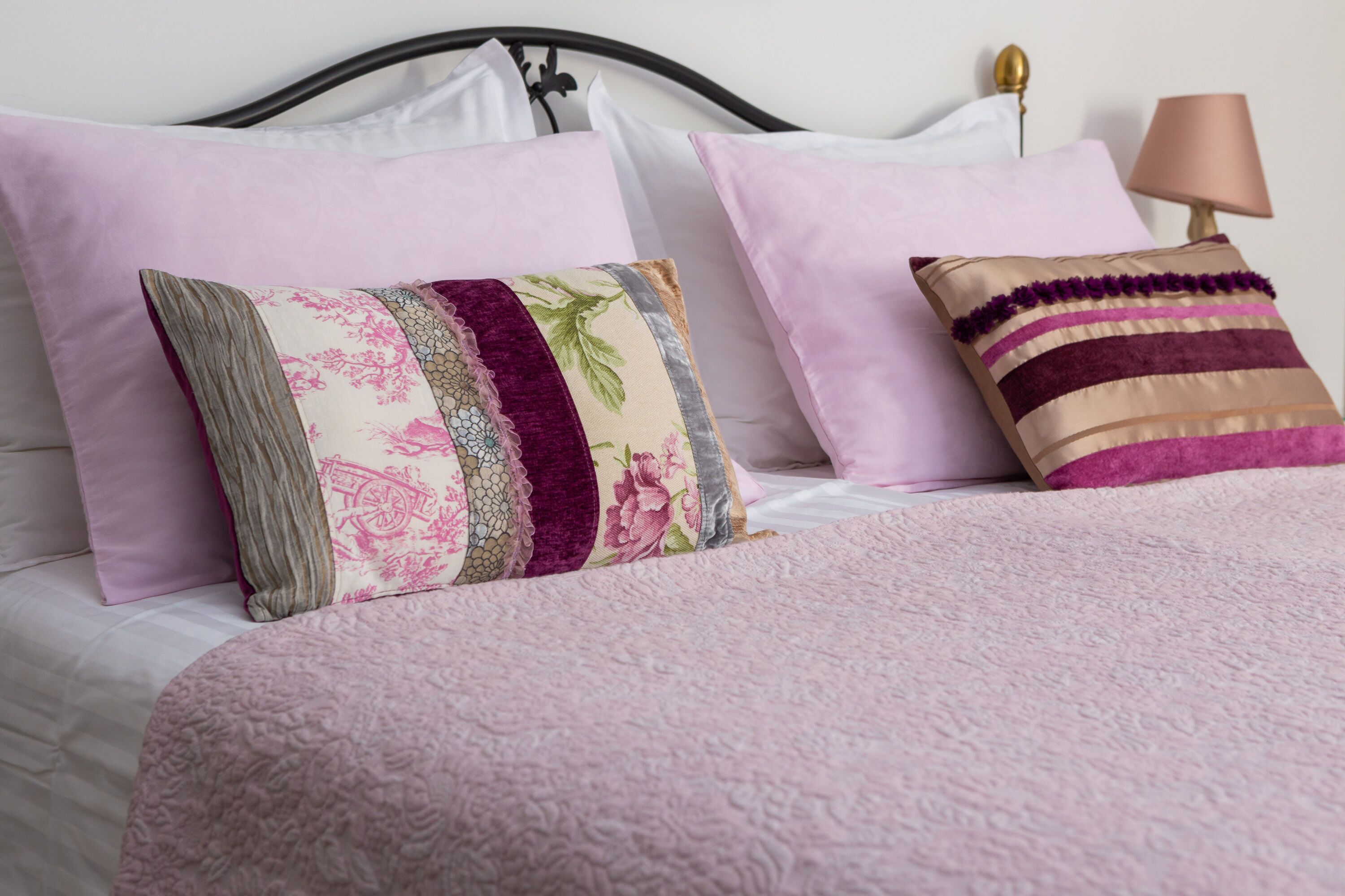 En seng med et pink pled og to dekorative puder.