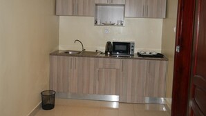 Cozinha compacta com armários de madeira, micro-ondas, pia e lixeira.