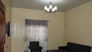Uma sala de estar com sofá, duas poltronas, televisão e lustre.