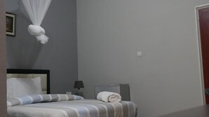 Quarto de hotel com cama, mesa de cabeceira, abajur, toalha enrolada e mosquiteiro.