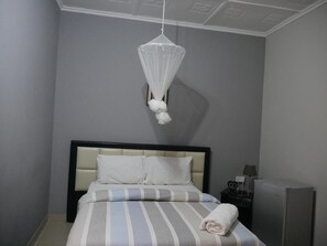 A bedroom with a bed, a nightstand, a lamp, and a hanging mosquito net.