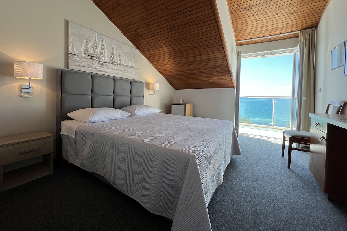 A bedroom with a large bed, a desk, and a view of the sea.