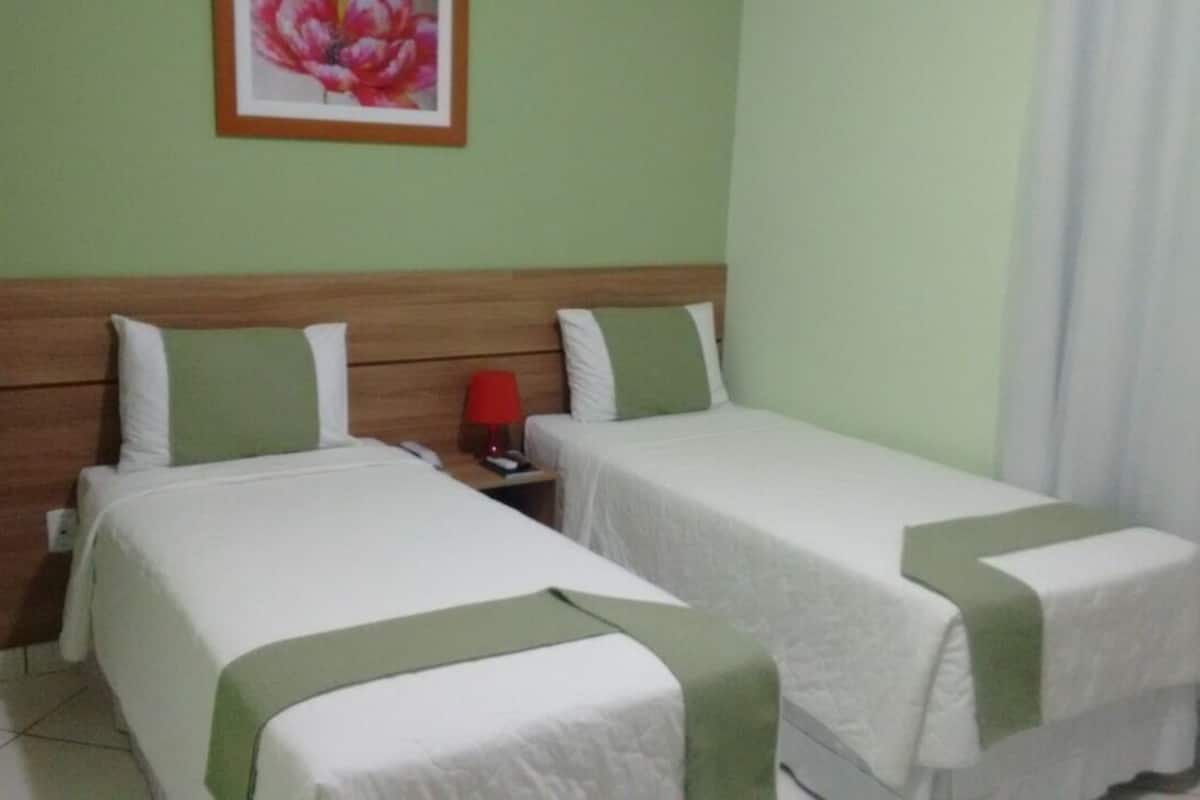 Une chambre d’hôtel avec deux lits simples, une tête de lit en bois, une lampe rouge et une œuvre d’art florale encadrée accrochée au mur.