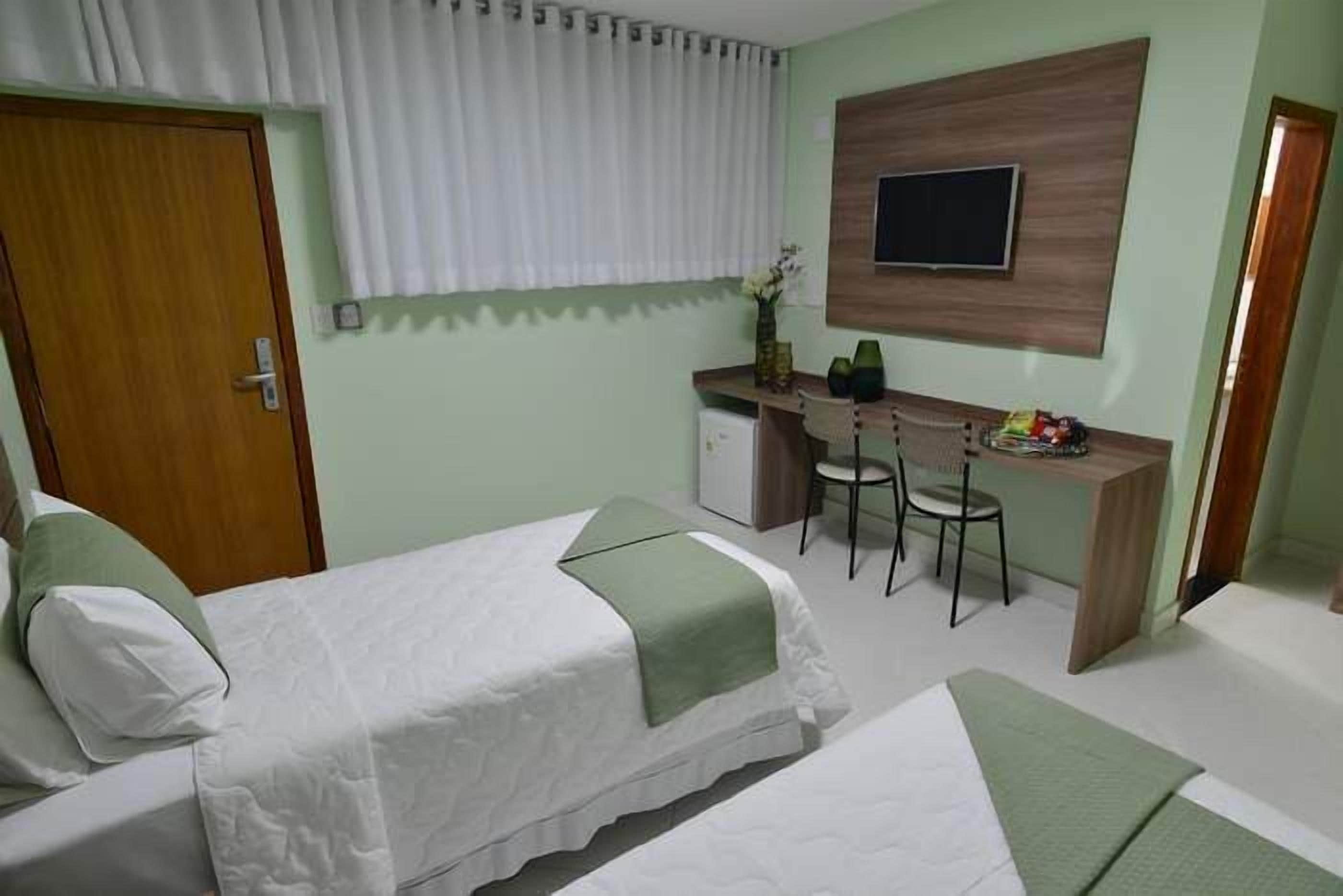 A hotel room with two beds, a desk with a chair, a television on the wall, and a door.