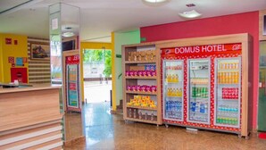 Een hotel receptie met een receptiebalie, een Domus Hotel bord en automaten met drankjes.