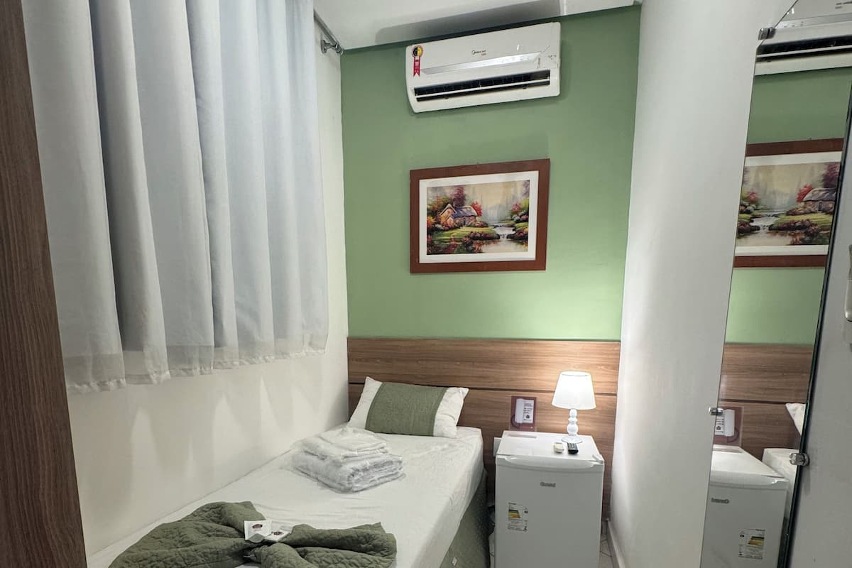 Une chambre d’hôtel avec un lit, un climatiseur, un tableau, une table de chevet avec une lampe et un miroir.