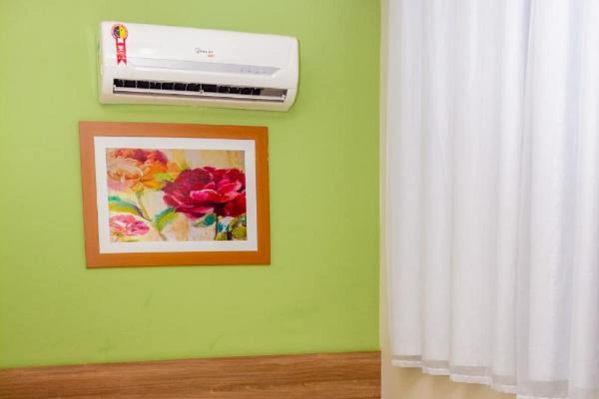 Ein Einzelbett mit einem grünen Handtuch, ein weißer Nachttisch mit einer roten Lampe und eine Wand-Klimaanlage.