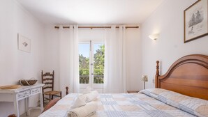 A bedroom with a wooden bed, a desk with a chair, a window with curtains, and a framed picture on the wall. - Villa Can Odile By SunVillas Mallorca (Cala San Vicens)