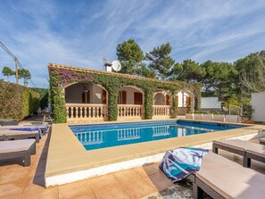 Un espace aménagé au bord de la piscine, comprenant une piscine, des chaises longues et un patio couvert agrémenté d’arches et de verdure.