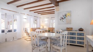 A spacious living area with a wooden ceiling, a round dining table surrounded by chairs, and a blue and white patterned sofa. - Villa Can Odile By SunVillas Mallorca (Cala San Vicens)