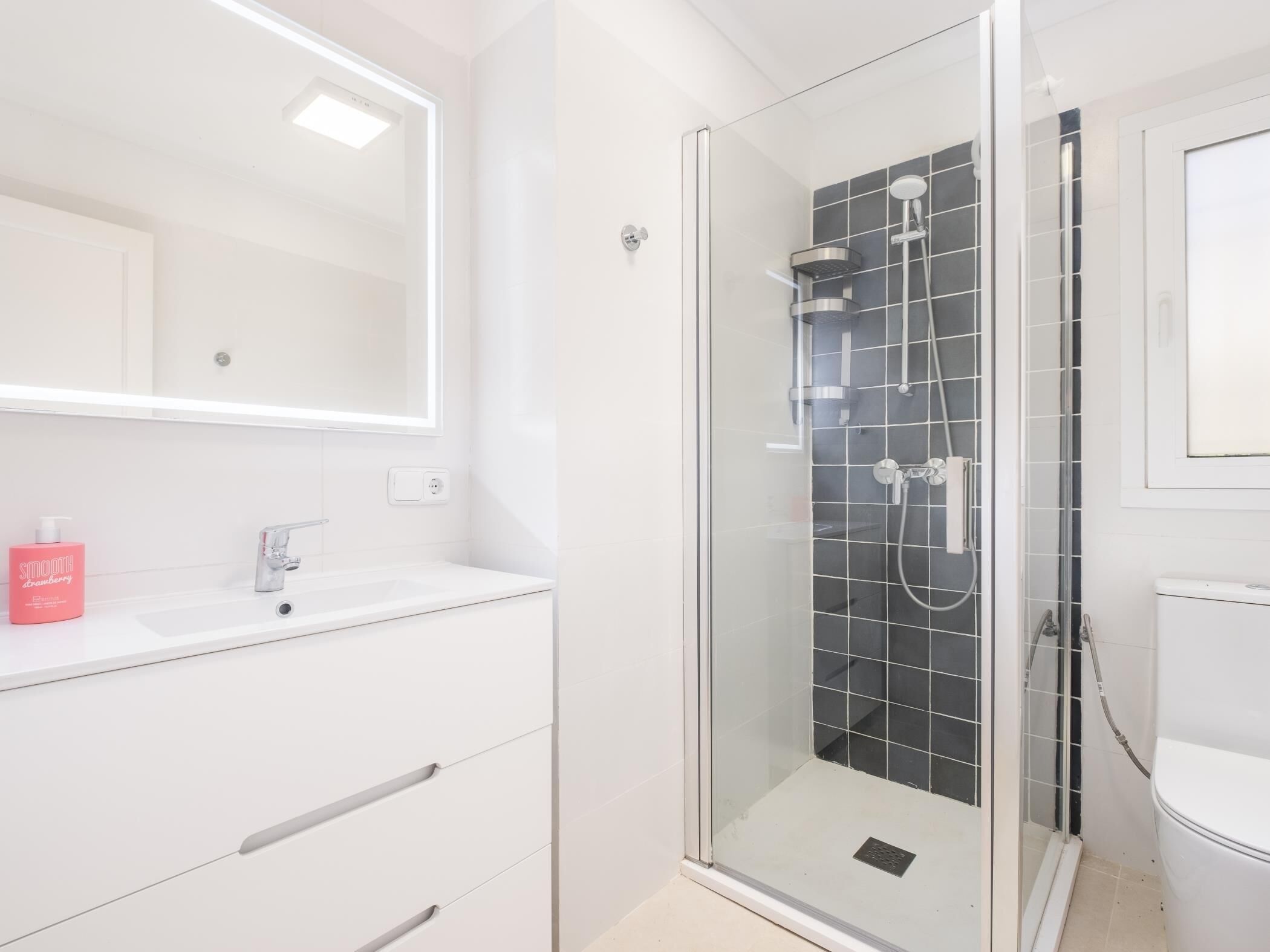 Un baño moderno con ducha envuelta en vidrio, tocador blanco y un espejo grande.