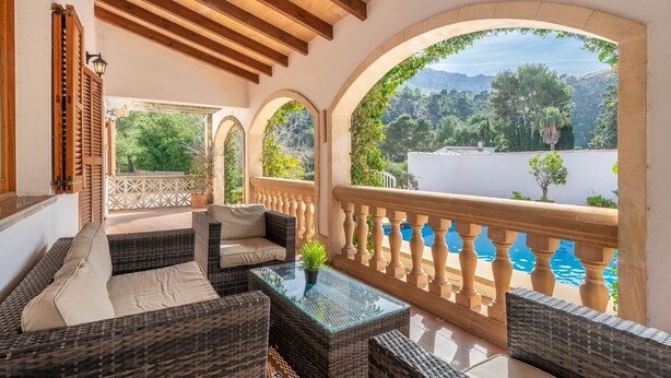 A balcony with wicker furniture, a glass table, and a view of a pool and mountains. - Villa Can Odile By SunVillas Mallorca (Cala San Vicens)