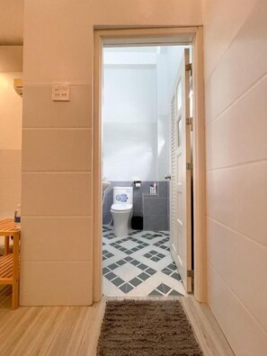 A hallway leading to a bathroom with a toilet, a sink, and a mirror. - B Home - Hostel (Can Tho)