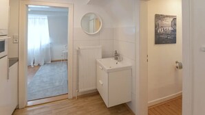 Une pièce moderne et bien éclairée, avec un plancher en bois, un radiateur blanc, un lavabo et un miroir au mur.