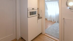 Une cuisine compacte dotée d’un four et d’un micro-ondes encastrés, d’un petit plan de travail et donnant sur une chambre à coucher par une porte.