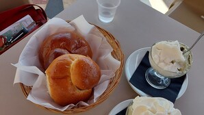 Een tafel met een mandje broodjes, twee schalen toetjes en een glas water.