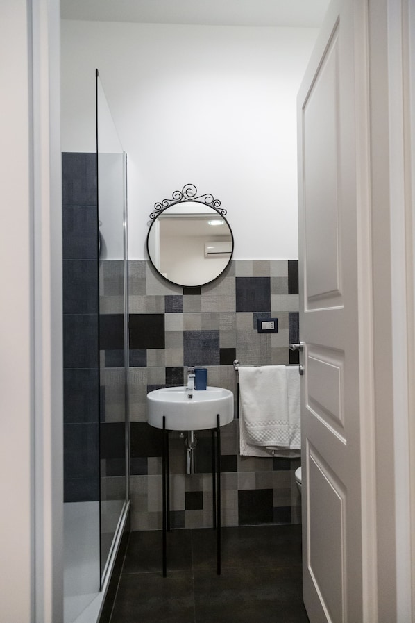 A bathroom with a glass shower enclosure, a white sink, and a tiled backsplash. - B&B A casa da Gabry (Catania)