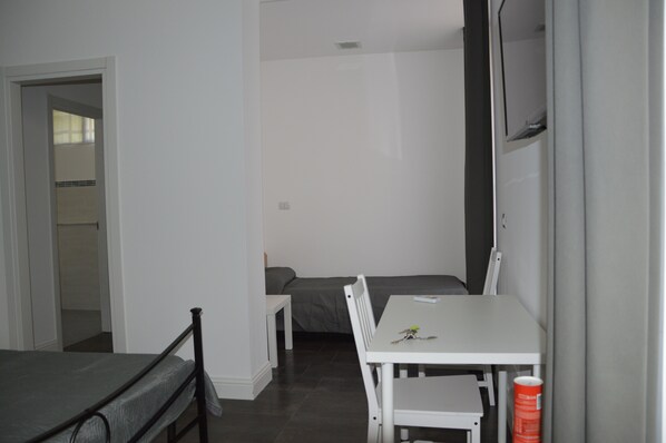 Una habitación pequeña y escasamente amoblada con una cama individual, una mesita y una silla.