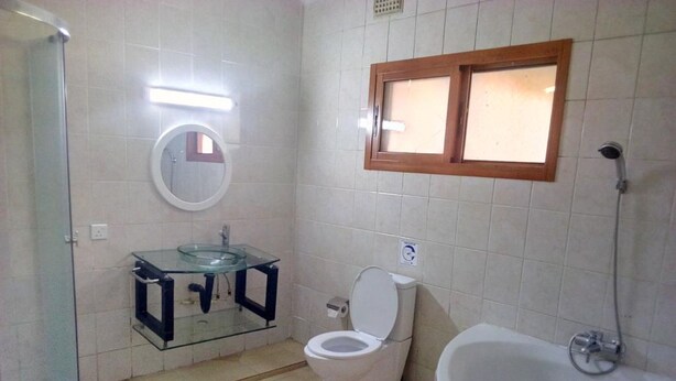A bathroom with a glass sink, a toilet, and a bathtub.