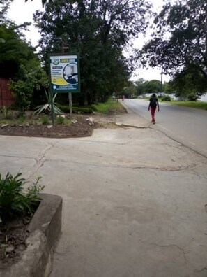 A road sign with a map and text, a sidewalk, and a pedestrian walking away. - Zenith lodge (Lusaka)
