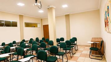 Un salón de conferencias con filas de sillas y mesas verdes, un proyector y un armario de madera.
