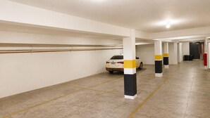 A parking garage with white walls, yellow lines on the floor, and pillars with yellow and black stripes. - Domus Hotel Veneza - Ipatinga (Ipatinga)