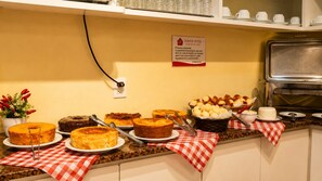 Ein Buffet mit verschiedenen Kuchen und Gebäck, ein Schild mit Rauchverbot und eine rot-weiße Karotischdecke.