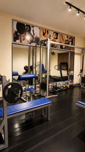 Uma academia com equipamentos de musculação, bancos e um espelho grande na parede.