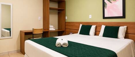 Quarto de hotel com cama, guarda-roupa de madeira, uma cadeira e um quadro na parede.