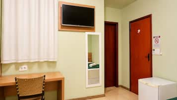 Ein Zimmer mit einem Holztisch, einem darüber montierten Fernseher, einem Spiegel, einer Tür mit einem AVISO-Schild und einem kleinen Kühlschrank.
