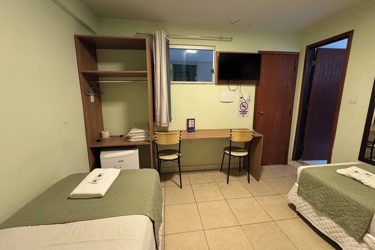 A room with two beds, a desk with a chair, a small kitchenette, and a door leading to another room.