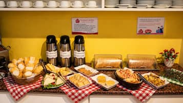 Disposição de buffet com diversos alimentos, incluindo pães, sanduíches e doces, sobre uma toalha xadrez.