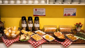 Montaje de bufé con diferentes opciones de comida, incluyendo pan, sándwiches y pasteles, sobre un mantel a cuadros.
