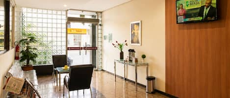 A hotel lobby with a reception desk, seating area, and a television screen displaying an advertisement.