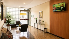 A hotel lobby with a reception desk, seating area, and a television screen displaying an advertisement.