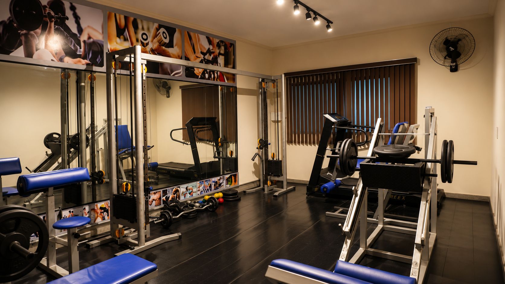 Uma academia com equipamentos de ginástica, esteira e espelho.