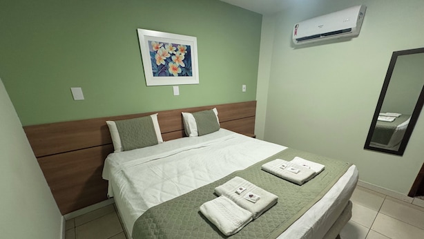 A neatly made bed with a green quilt, white bedding, and two folded towels on the bed. - Domus Hotel Veneza - Ipatinga (Ipatinga)
