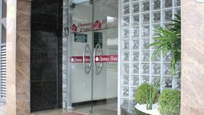 The entrance to Domus Hotel with a glass door, a red mat at the entrance, and a small planter with plants. - Domus Hotel Veneza - Ipatinga (Ipatinga)