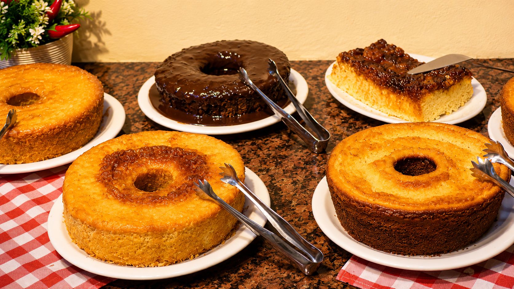 A variety of cakes on plates with forks, placed on a table with a checkered tablecloth.