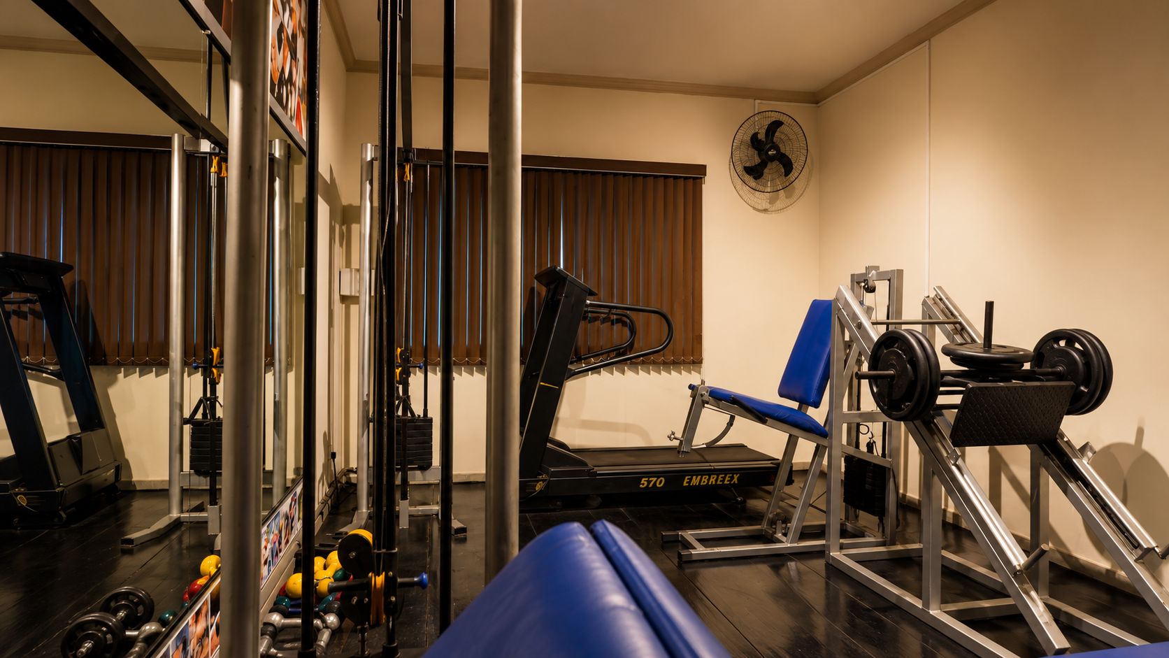 Un gimnasio con equipamiento de ejercicio, una cinta de correr y un banco de pesas.