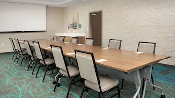 Un salón de conferencias con una larga mesa, sillas, una pantalla de proyector y piso alfombrado.