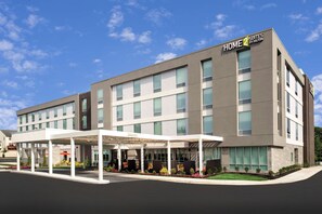 Un hôtel moderne doté d’une entrée couverte et d’une enseigne indiquant qu’il s’agit d’un Home 2 Suites de la chaîne Hilton.