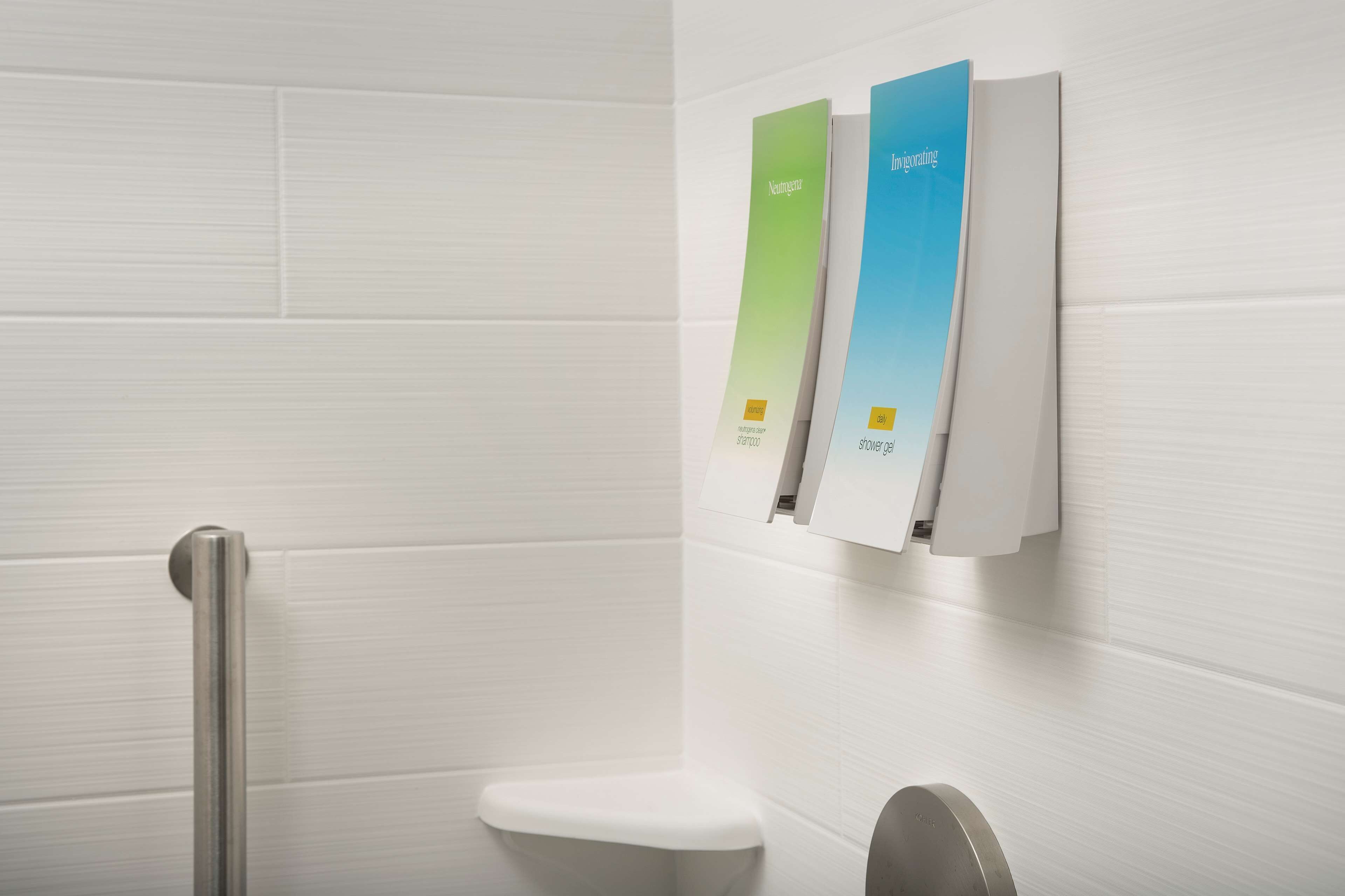 A bathroom with a white tiled wall, a white toilet, and a handrail. There are three vertical panels on the wall, each with a label and a small yellow square.