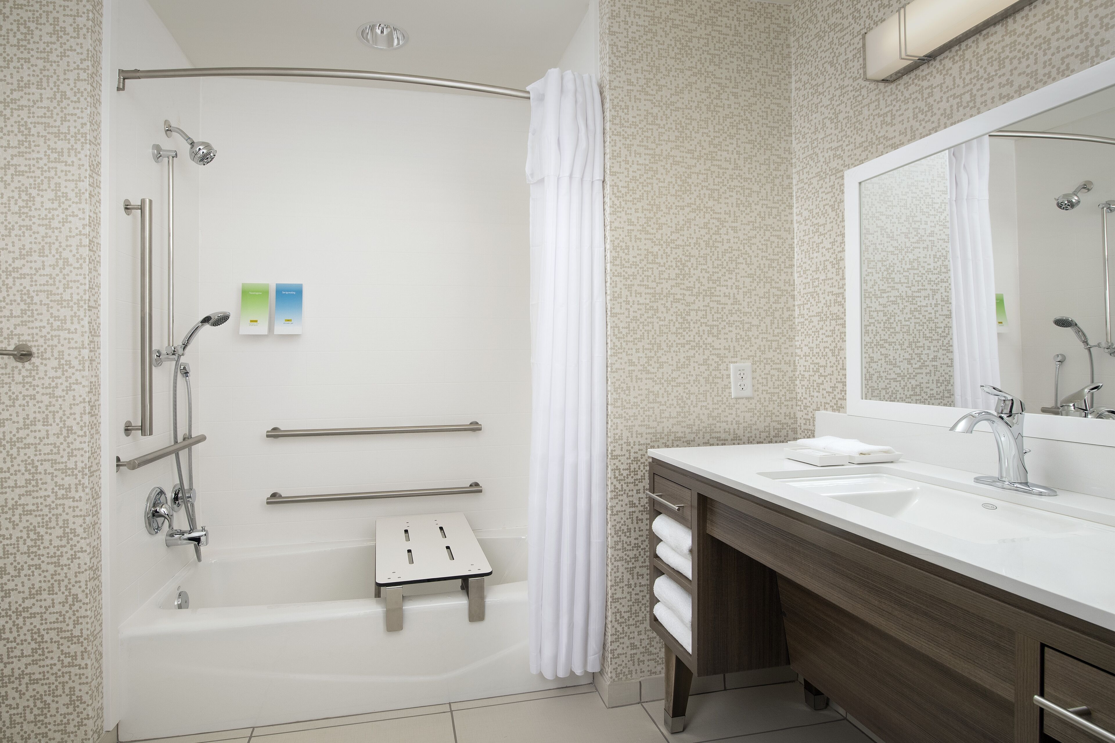 A modern bathroom with a walk-in shower, grab bars, a vanity with a mirror, and a bathtub.