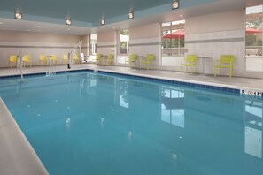 Une piscine avec des chaises et des tables jaunes, une échelle et une vue sur l’extérieur.