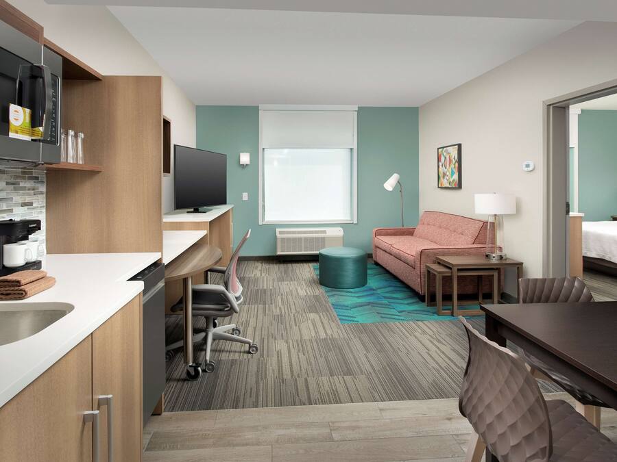 Une chambre d’hôtel moderne dotée d’une kitchenette, d’un téléviseur à écran plat, d’un canapé, d’une table à manger et d’une grande fenêtre.