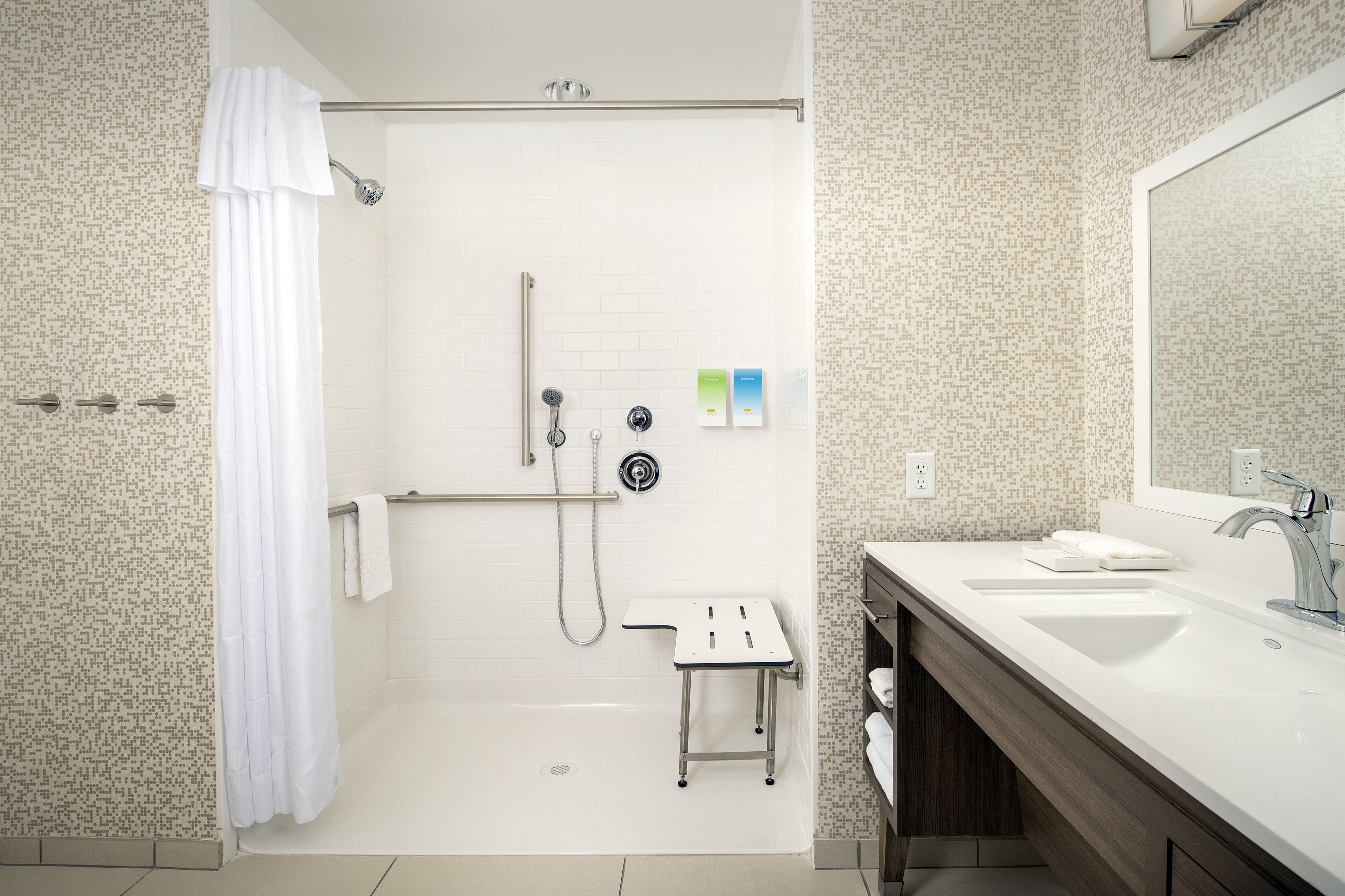 Un baño moderno con ducha, un taburete pequeño, un lavabo y un espejo.