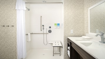 Un baño moderno con ducha, un taburete pequeño, un lavabo y un espejo.